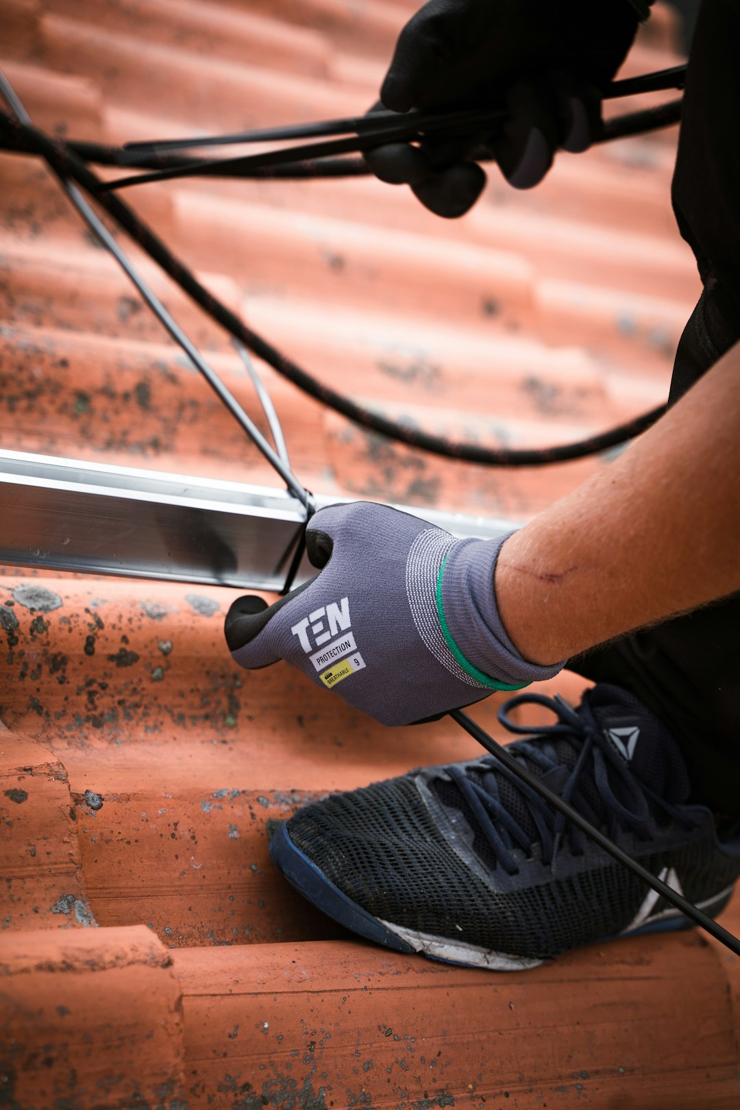 An electrician with work gloves making an solar panel installation on a roof